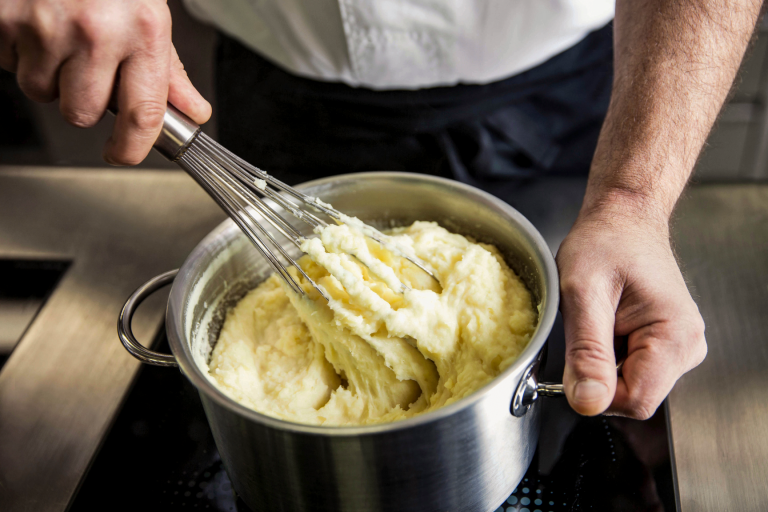 Manos del chef preparando puré de papas en una cacerola