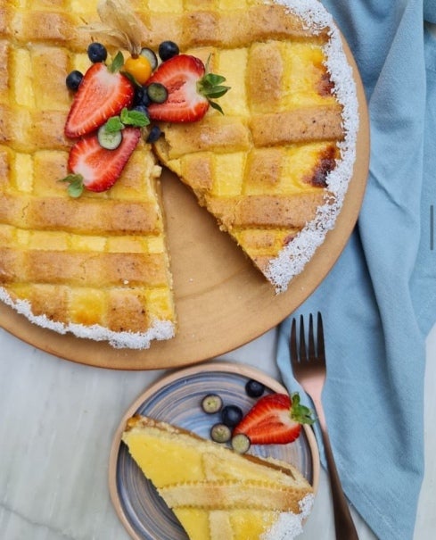 Tarta de ricotta y manjar Nestlé decorado con frutillas y borde de coco rallado junto a un plato con una porción de la tarta