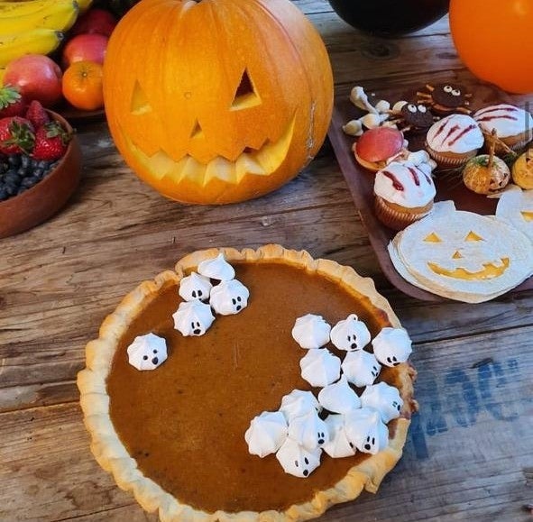 Pie de zapallo decorado con suspiros junto a una calabaza de Halloween, frutillas y golicinas