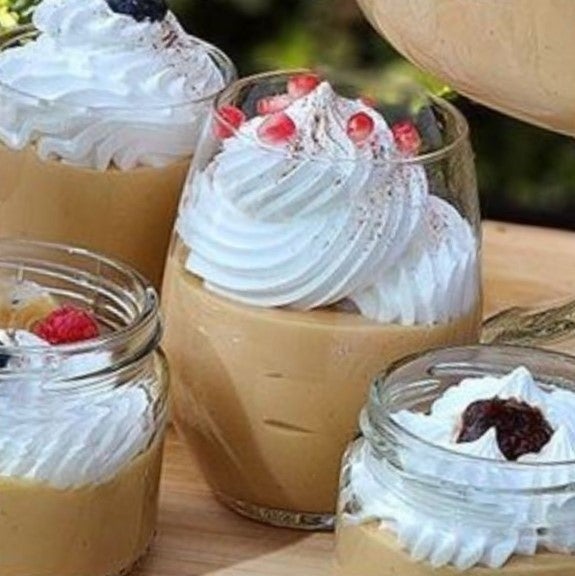 Cuatro vasos de vidrio con Suspiro limeño decorados con frutas, merengue y canela en polvo