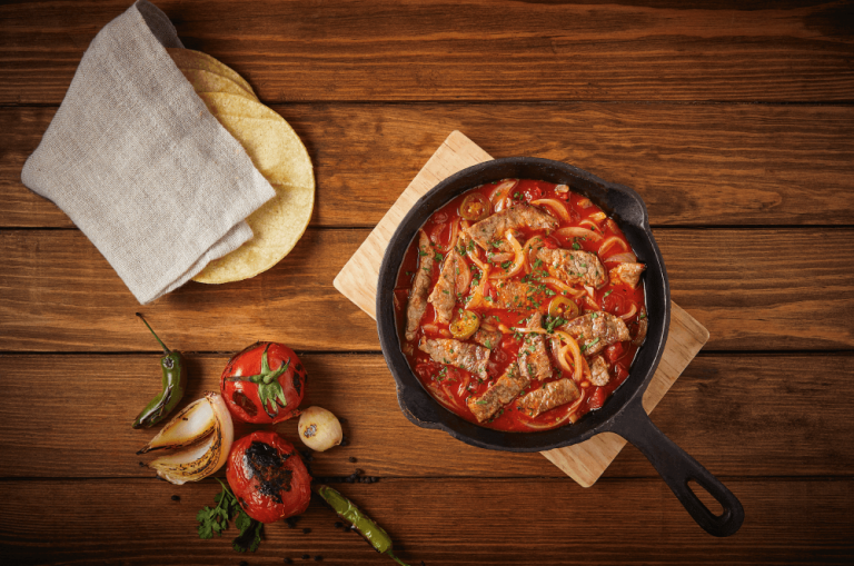 Estofado en sartén de hierro fundido junto a verduras rostizadas y tortillas de maíz