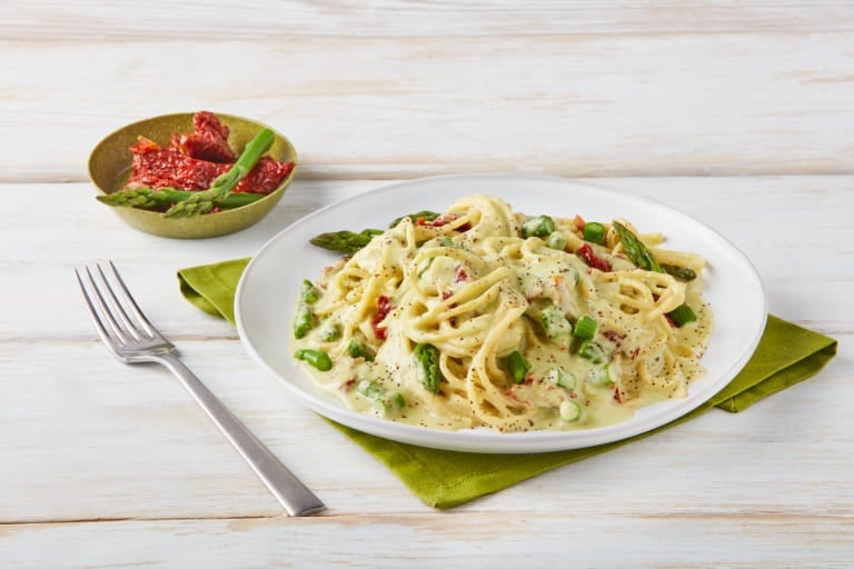 Plato de espaguetis con salsa de espárragos y tomates deshidratados sobre servilleta verde