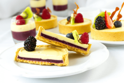 Tartaleta de Crème Brûlée bicolor partida a la mitad y servida en un plato y al fondo otros postres