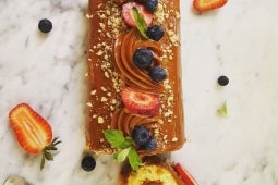 Brazo de reina decorado con fresas, arándanos y menta, cubierto con Manjar Nestlé y nuez, presentado en una mesa de mármol