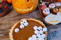 Pie de zapallo decorado con suspiros junto a una calabaza de Halloween, frutillas y golicinas