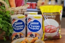 Guiso de mote y camarones junto a cajas de Crema de Leche y una bolsa de salsa de tomates deshidratada Maggi