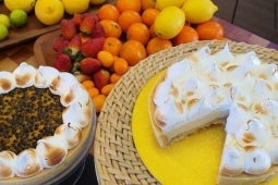 Pie de limón y maracuyá con merengue suizo junto a dos bandejas con limones, mandarinas y fresas