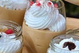 Cuatro vasos de vidrio con Suspiro limeño decorados con frutas, merengue y canela en polvo
