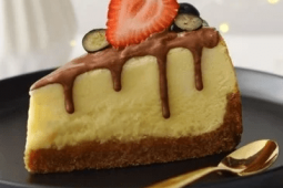 Porción triangular de Cheesecake de Kit Kat decorado con frutillas servido sobre un plato negro