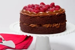 Sobre una mesa, torta de chocolate y manjar de dos capas decorada con frambuesas