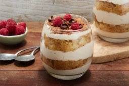 Dos vasos rellenos con un postre de tiramisú y decorado con chocolate y frambuesas