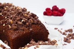 Keke SUBLIME® decorado con trozos y salsa de chocolate, al lado, una taza de frambuesas