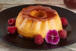 Crema Volteada Gourmet servida en un plato negro y decorada con NESTLÉ® Leche Condensada, flores y frambuesas