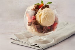 Un vaso de cristal con helado de vainilla, trozos de chocolate y frutos rojos, adornado con una ramita de menta.