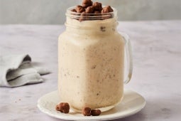 Batido cremoso en un frasco de vidrio cubierto con bolitas de chocolate, colocado sobre un platillo blanco.