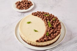 Cheese de queso con la mitad cubierta de racimos de chocolate, adornada con hojas de menta.