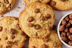 Galletas con chispas de chocolate sobre una superficie, al lado de un pequeño recipiente con Sublime Pops.