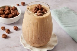 Batido cremoso cubierto con cereal de chocolate en un vaso, con más cereal en un tazón cercano.