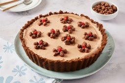 Pie de mousse de chocolate decorada con crema batida y frutos rojos, sobre un plato celeste.