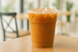 Vaso Transparente NESCAFÉ con receta Cacao Con Leche Hot Over Ice sobre una mesa de una confiteria