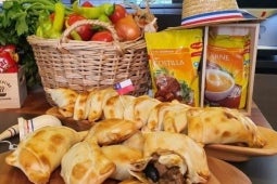 Empanadas de pino al horno sobre tablas de cortar, al fondo canasta de verduras y productos MAGGI®