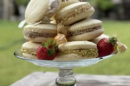 Alfajores de maicena decorados con coco y pistacho sobre un plato de vidrio con fresas