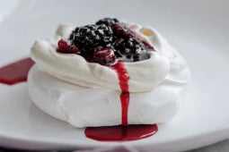 Servido en un plato, Pavlova con Crema Chantilly y Salsa de Berries