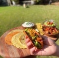 Mano sosteniendo un taco con sofrito de Awesome Burger, tomates, cilantro picado, porotos negros y gajos finos de palta