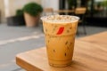  Vaso Transparente NESCAFÉ con receta Cappuccino Hot Over Ice sobre una mesa en el exterior de una cafetería