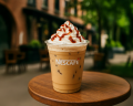 Vaso de plástico transparente con el logo de Nescafé, lleno de café helado con hielo, coronado con crema batida.