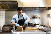 En una cocina comercial, chef empaca una preparación en una caja para ser enviada como entrega a domicilio