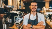 Dueño de un negocio de café-bar sonriendo con los brazos cruzados