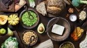 Variedad de alimentos vegetales como tofu, legumbres, frutos secos y harinas integrales sobre una mesa rústica