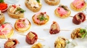 Variedad de canapés decorados con crema, eneldo, frutos rojos y carnes frías, dispuestos sobre una bandeja