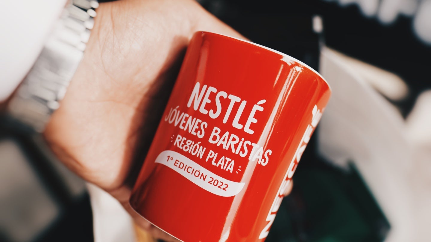 Mano sosteniendo taza de café que dice "Nestlé Jóvenes Baristas Región PLATA 1° Edición 2022"
