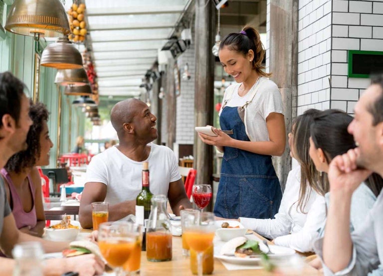 Mesera toma la orden de un grupo de comensales en un restaurant y comunica la presencia de alérgenos alimentarios
