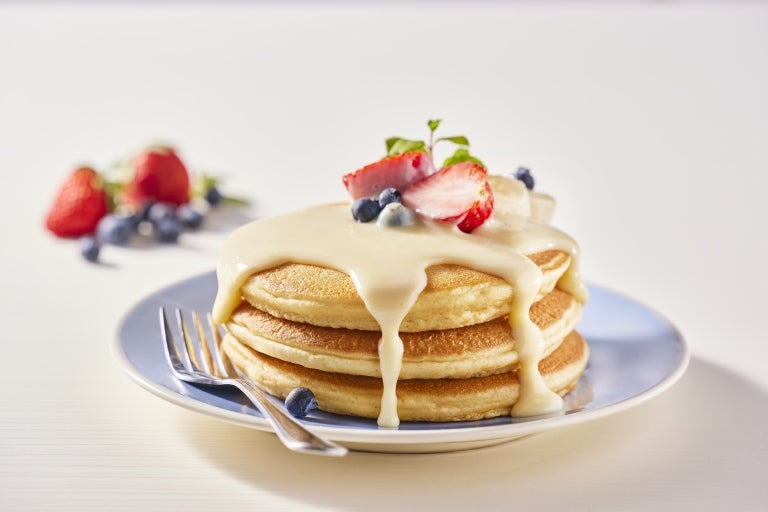 3 hot cakes sobre un plato cubiertos con leche condensada y frutos rojos