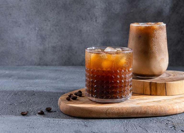 Sobre una tabla con dos niveles se ubican dos vasos diferentes con bebidas de café frío preparadas de forma distinta