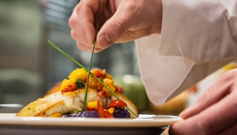 Cocinero emplatando su platillo delicadamente en un servicio de catering.
