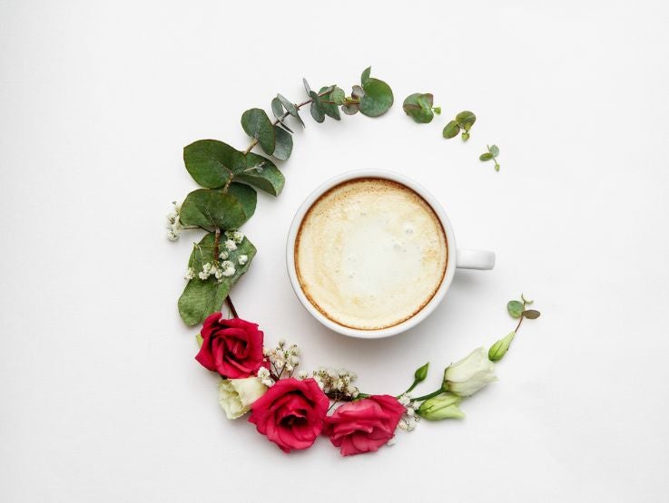 Taza de café preparada con bebida vegetal y rodeada de flores y hojas naturales