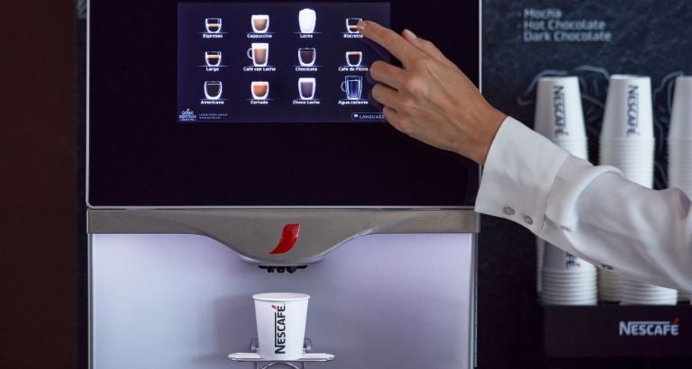 Mano seleccionando bebida en pantalla táctil de máquina de café con vaso debajo