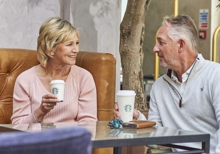 Pareja de adultos mayores conversando en lounge de hotel mientras disfrutan café caliente.