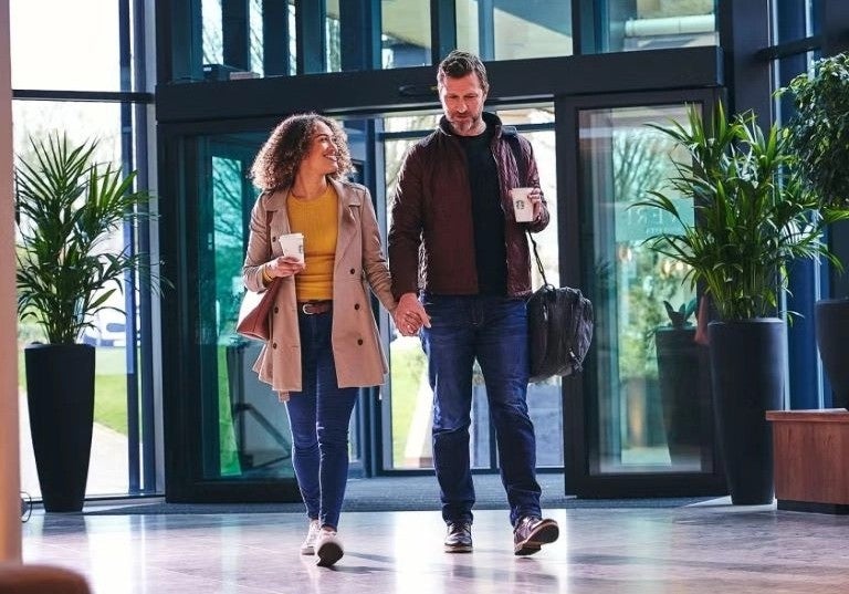 Pareja caminando en edificio moderno mientras disfruta café para llevar.