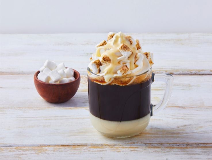 Vaso de café bombón, crema batida y pequeños malvaviscos dorados encima.