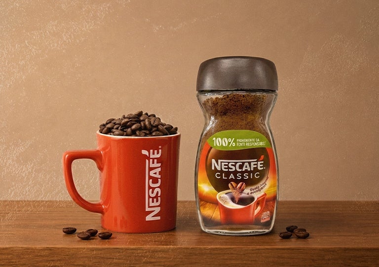 Frasco de café soluble junto a taza roja de NESCAFÉ® con granos de café
