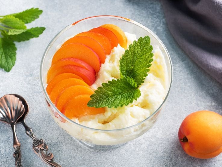 Postre de crema blanca y rodajas de durazno y decorado con hojas de hierbabuena