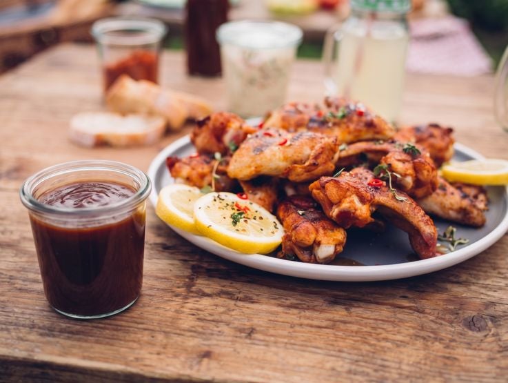 Alitas de pollo bañadas en salsa espesa tipo BBQ con brillo, presentadas en plato metálico