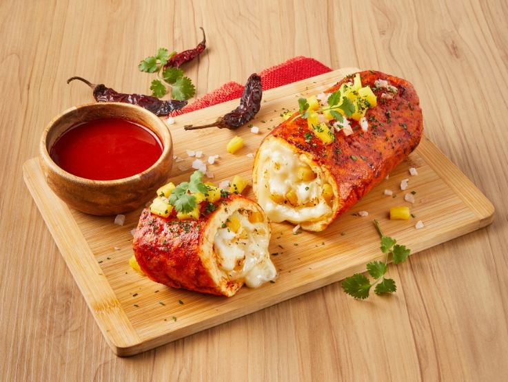 Rollos rellenos con queso derretido y salsa roja, decorados con hierbas sobre una mesa de madera