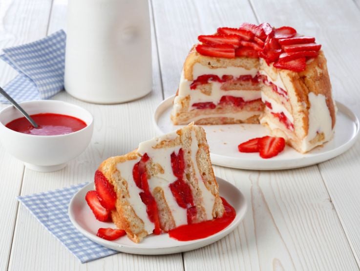 Porción de carlota de fresa con crema servida en plato junto al pastel entero y salsa dulce.