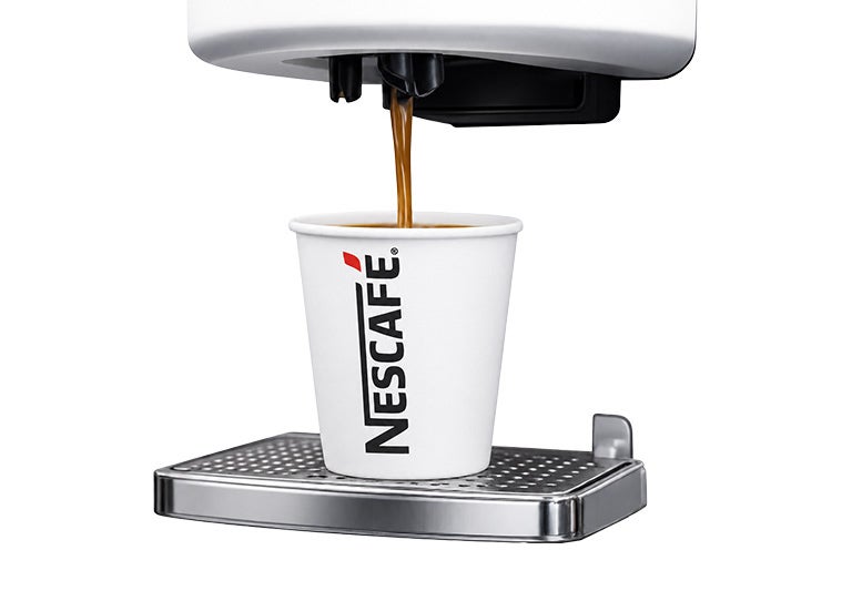 Máquina dispensando café en vaso con logotipo NESCAFÉ sobre bandeja metálica